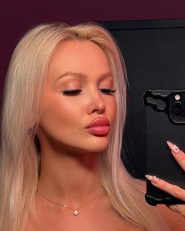 Bimbo glow-up mirror selfie with long platinum hair, long nails and soft glam makeup.