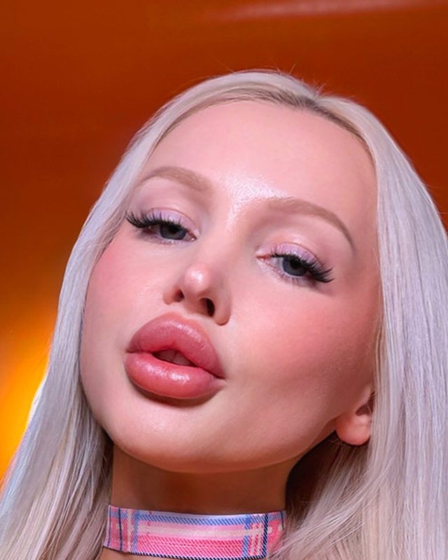 Close-up of glossy overlined bimbo lips with a pink plaid choker and platinum hair.