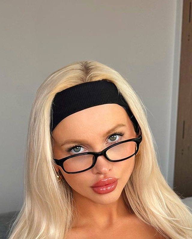 Nerdy bimbo look with black rectangular glasses, a black headband and platinum blonde hair.